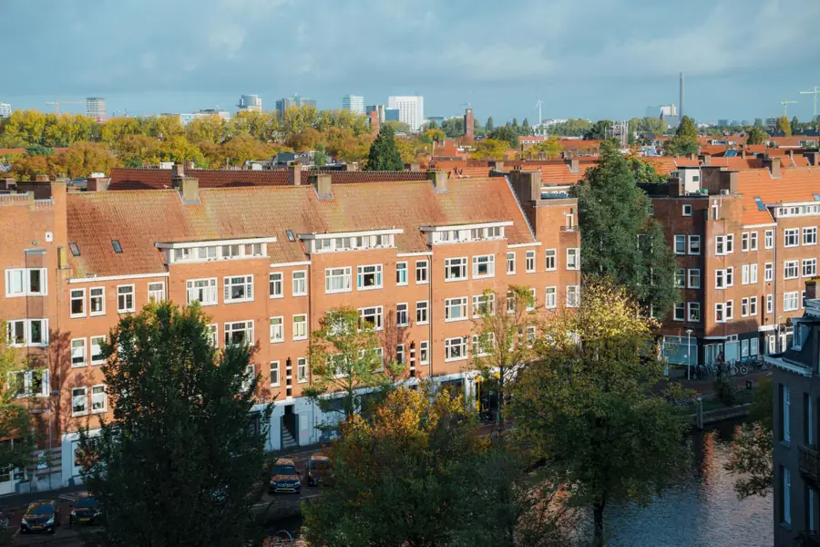 Amsterdamse woonblokken van rode baksteen met pannendaken en dakkapellen langs een gracht, met de skyline op de achtergrond