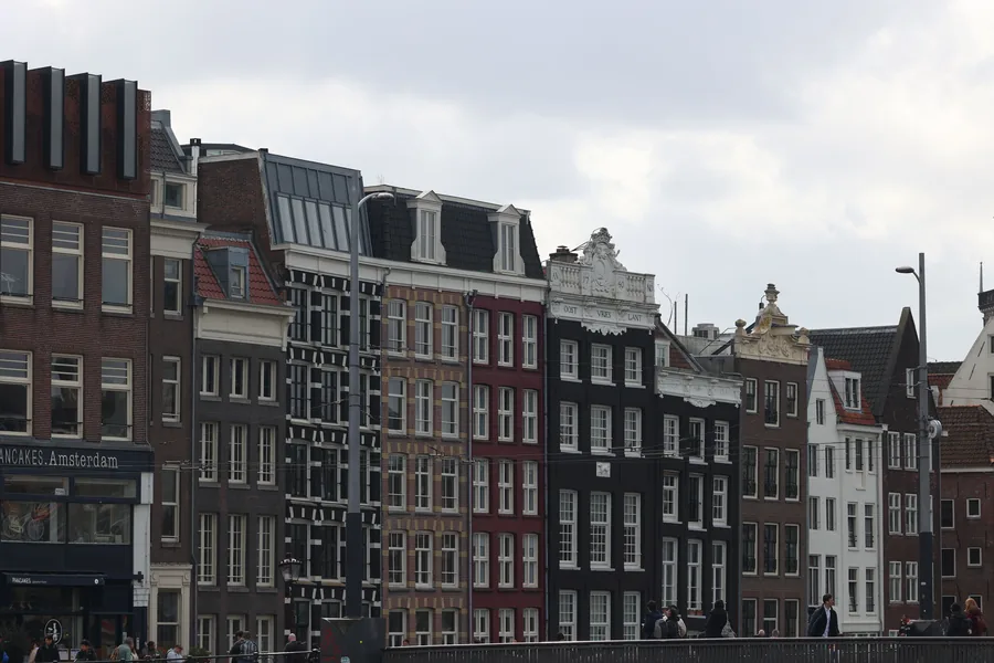 Rij Amsterdamse grachtenpanden met verschillende gevels, dakkapellen en een glazen dakopbouw aan de straatkant