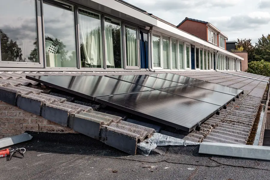 Zonnepanelen op een dak van rijtjeswoningen naast een strook dakpannen en een plat dakdeel